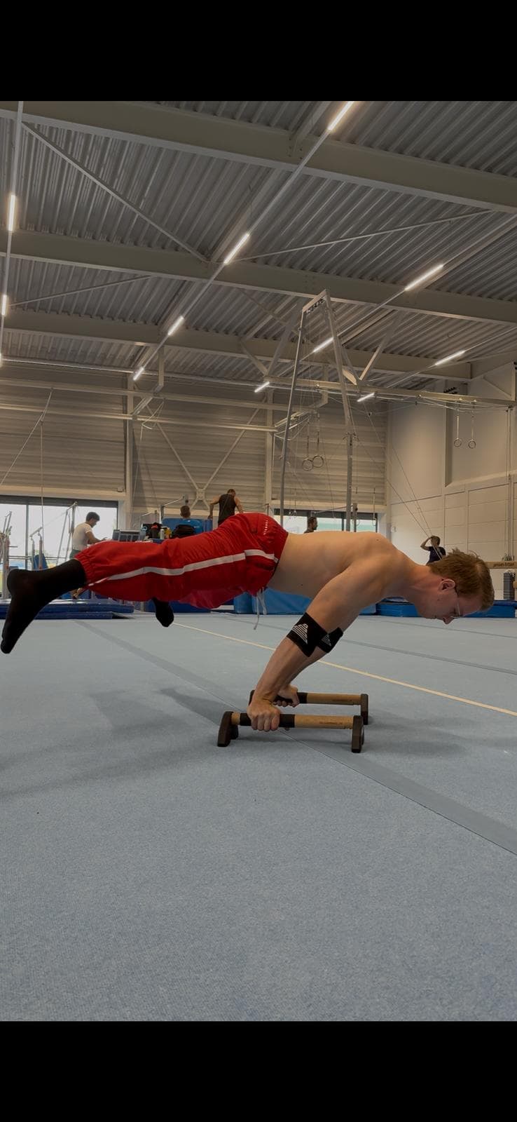 Tim in een planche op parallettes in de turnhal, voeten los van de grond
