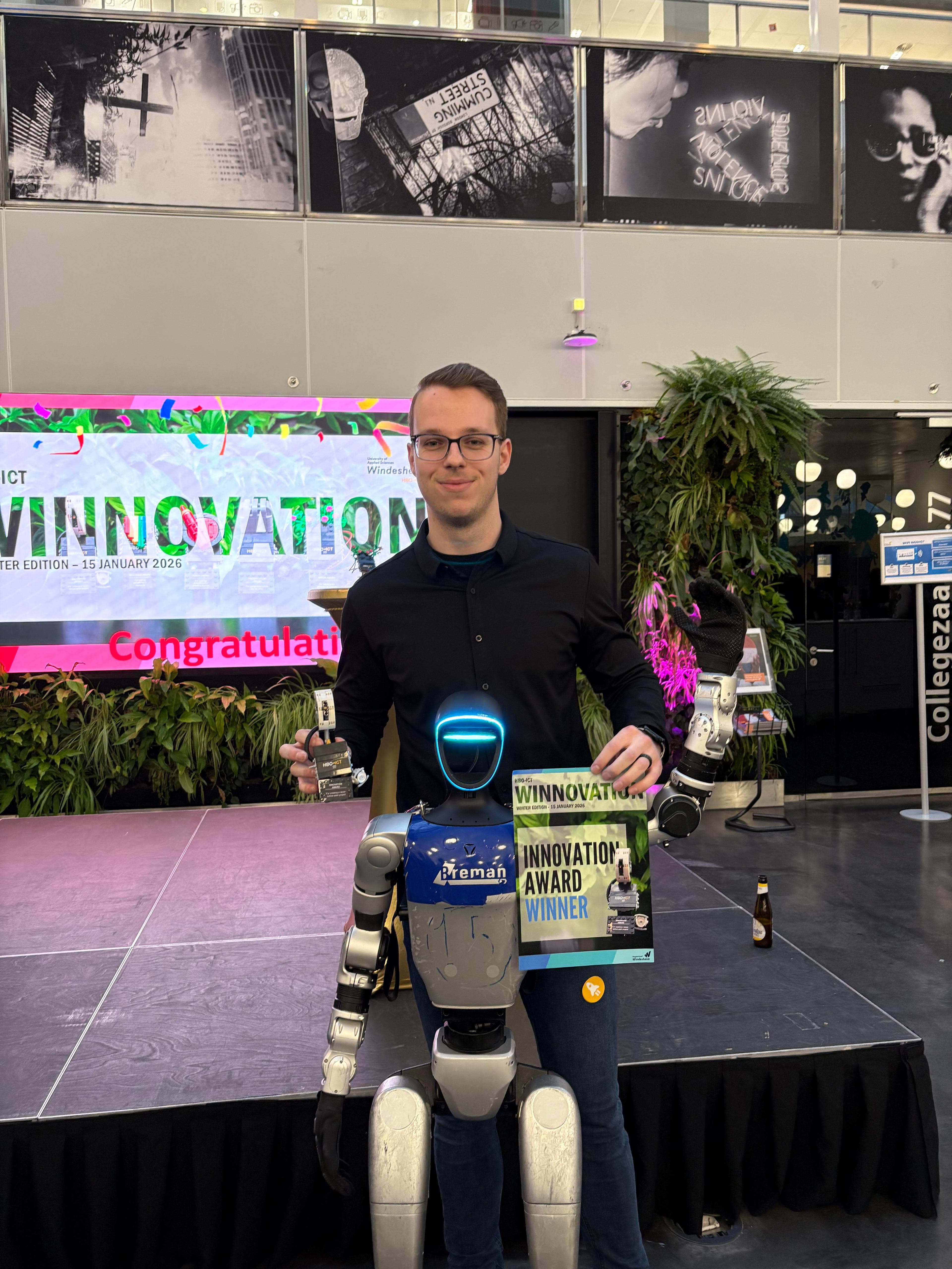 Tim met de Innovation Award in zijn hand, achter een humanoïde robot op het Winnovation-evenement